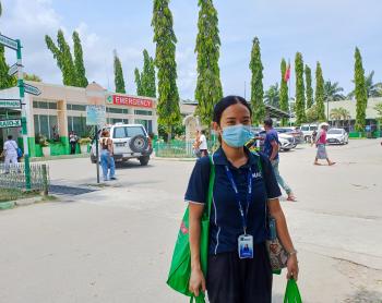 A woman stands outside a hospital with shopping bags