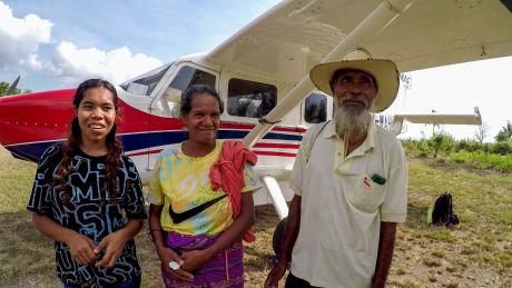 Three people stand by a small plane