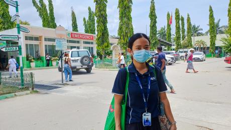 A woman stands outside a hospital with shopping bags