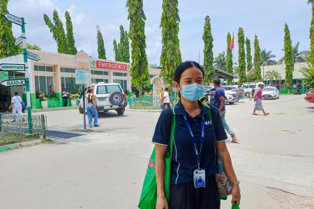 A woman stands outside a hospital with shopping bags