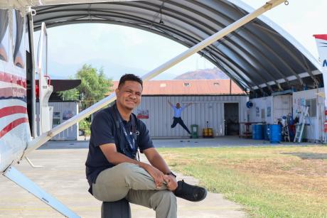 A man sits on a plane's wheel posing for a photo