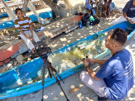 A man films a fisherwoman in a beachside village
