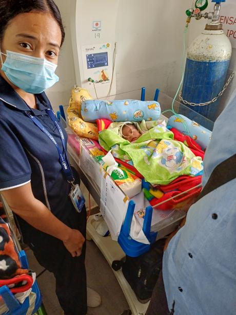 A woman stands next to a premature baby in an incubator