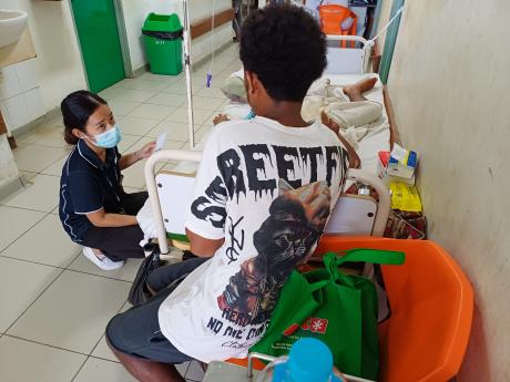 A woman crouches by a hospital bed, visiting patients