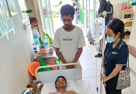 Vincencio receives treatment in a hospital ward in TImor-Leste while his brother stands nearby and MAF chaplain, Ingrrid Pinto, stands beside the bed.